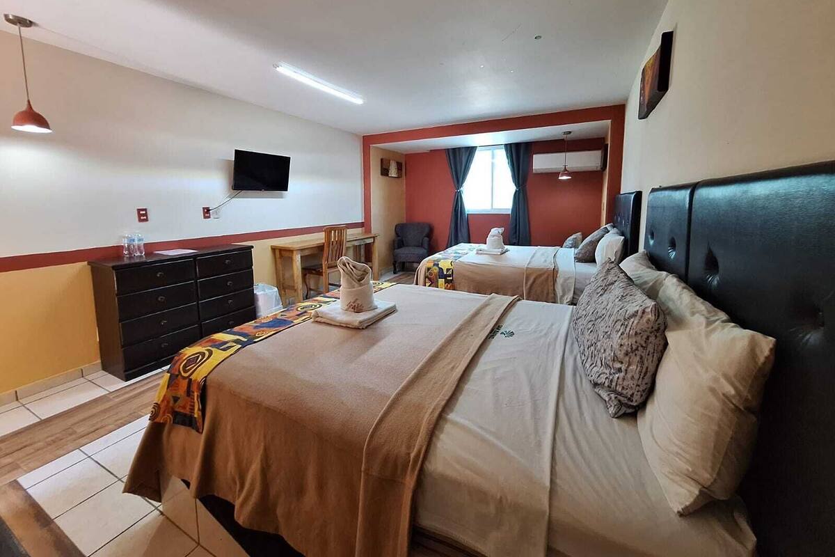 A hotel room with two beds, a desk, a chair, a television, and a dresser.
