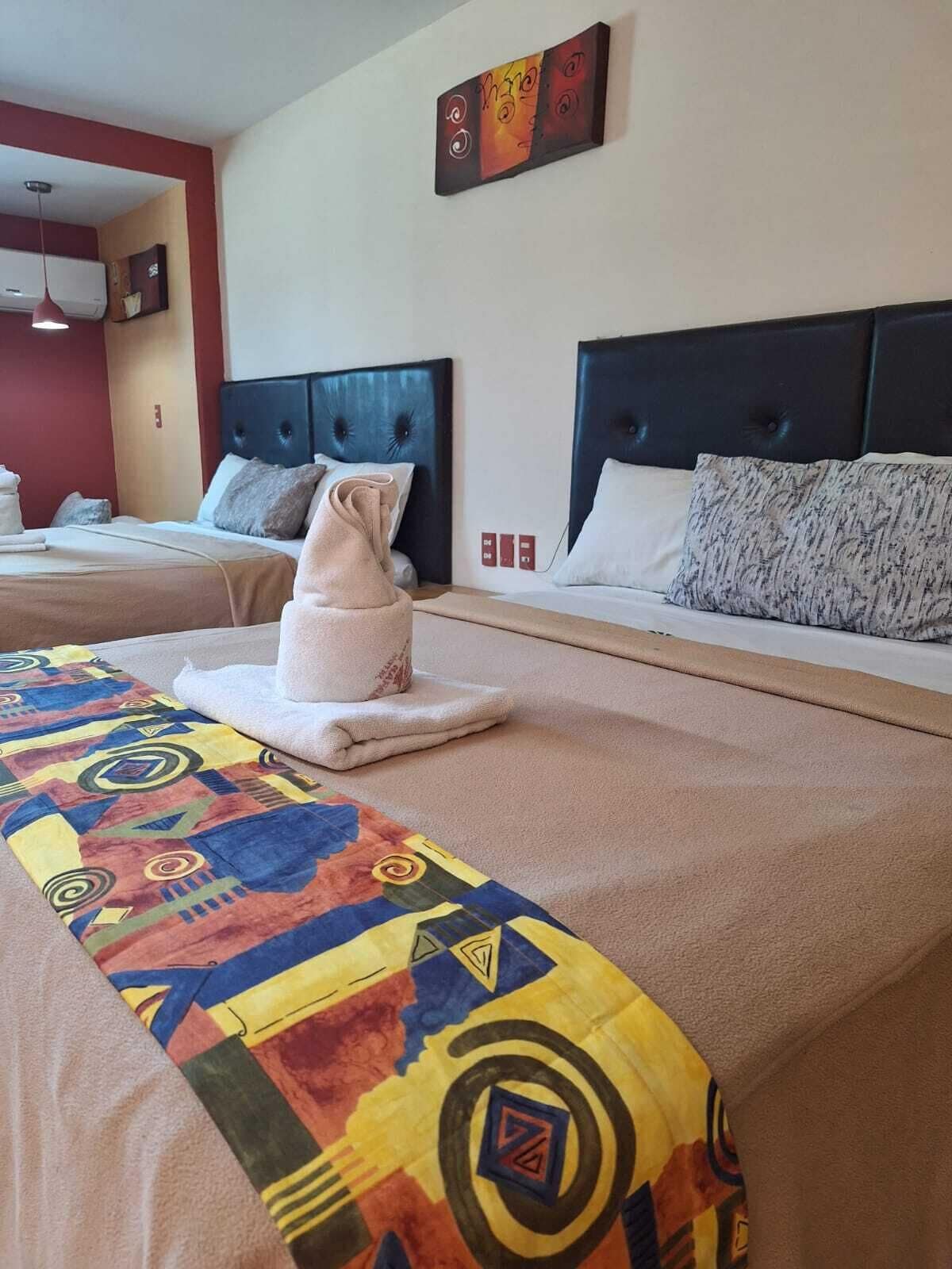 A hotel room with two beds, each with a headboard and pillows. There is a colorful blanket on the bed in the foreground.