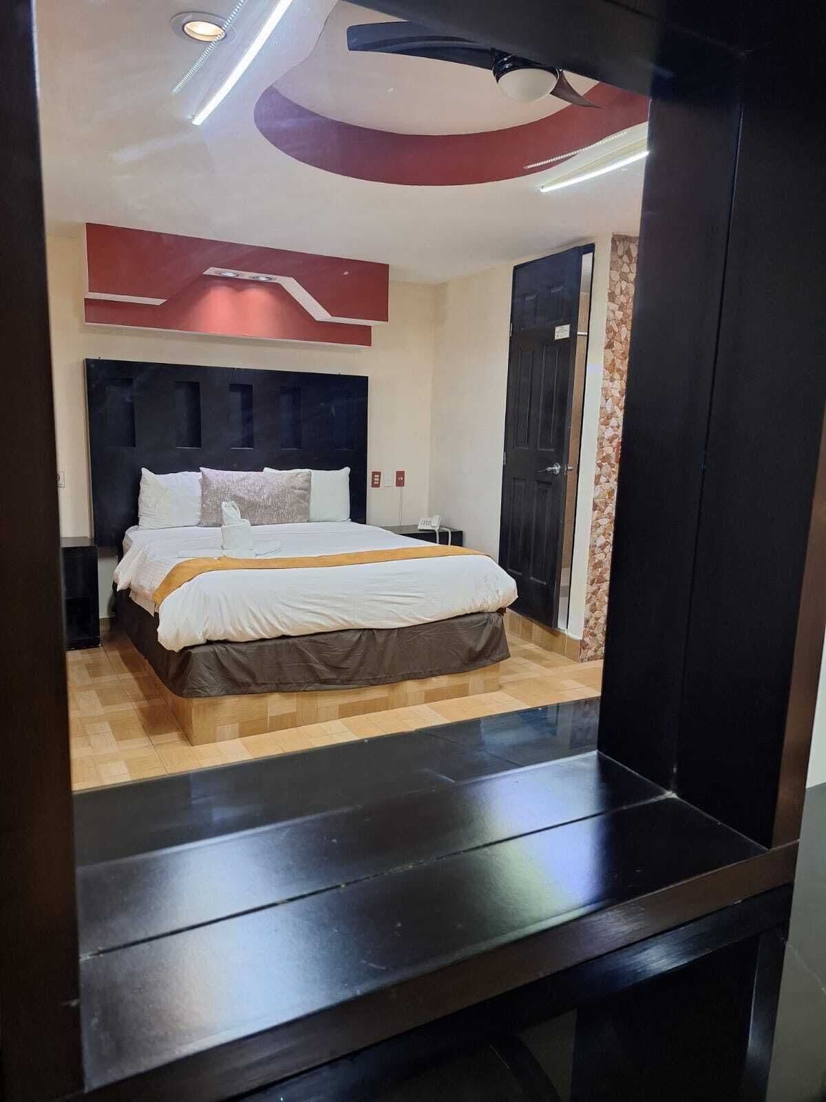 Ett modernt hotellrum med en stor säng, en mörk sänggavel och ett trägolv.