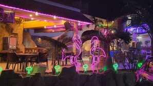 An outdoor dining area with neon flamingo decorations, palm trees, and a covered seating area. - Hotel San Rafael Poza Rica (Poza Rica)