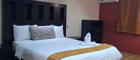 Quarto de hotel com uma cama grande, cabeceira escura, ar condicionado fixado na parede e piso de madeira.
