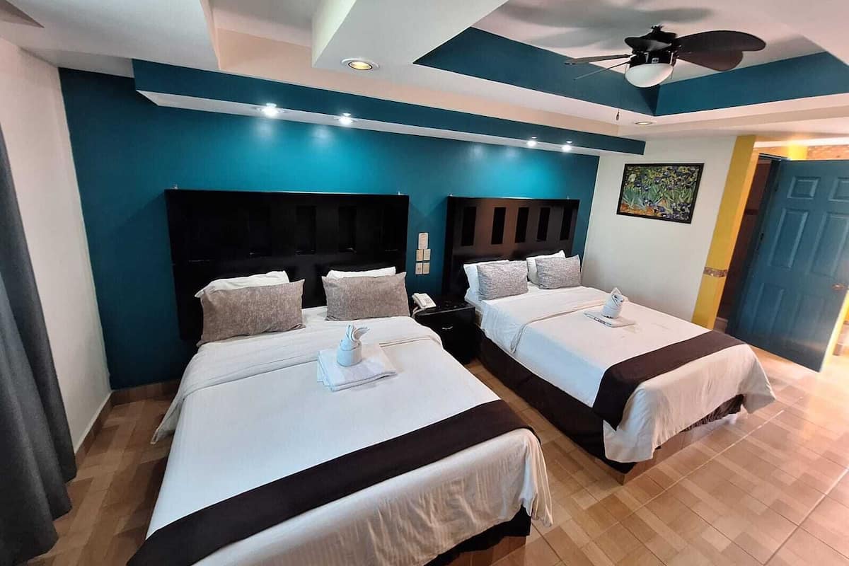 A hotel room with two beds, a ceiling fan, and a painting on the wall.