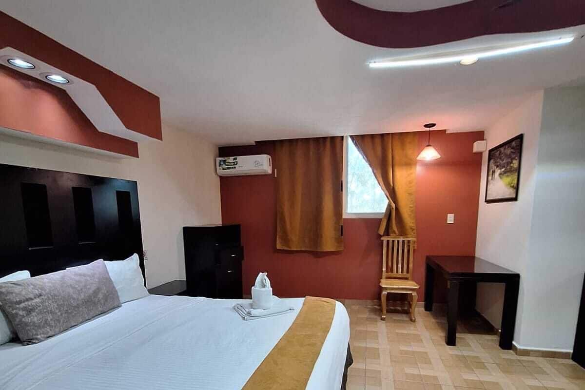 A hotel room with a large bed, a wooden chair, a small table, and a wall-mounted air conditioner.
