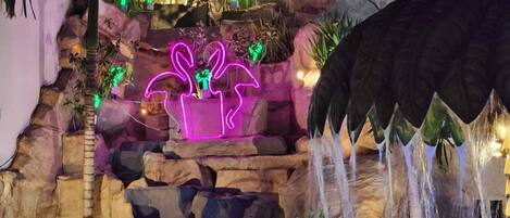 A rock garden with cascading water feature and neon-lit potted plants.