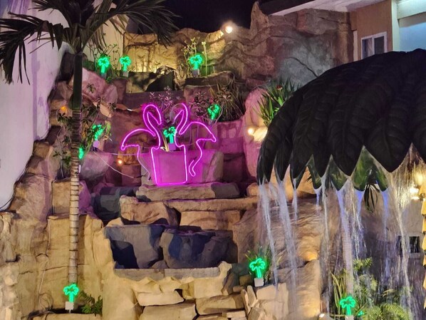 A rock garden with cascading water feature and neon-lit potted plants.