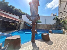 Una piscina con tobogán, rodeada de muros de piedra y una palmera.