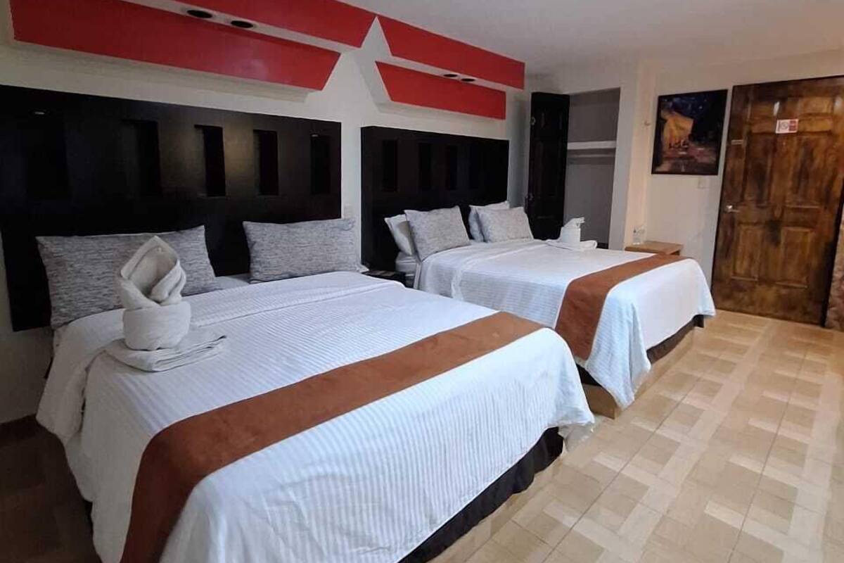 A hotel room with two beds, each with a white bedspread and a brown accent. The room has a tiled floor and a red and white ceiling design.