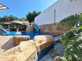 A swimming pool with a slide, palm trees, and a rock formation.