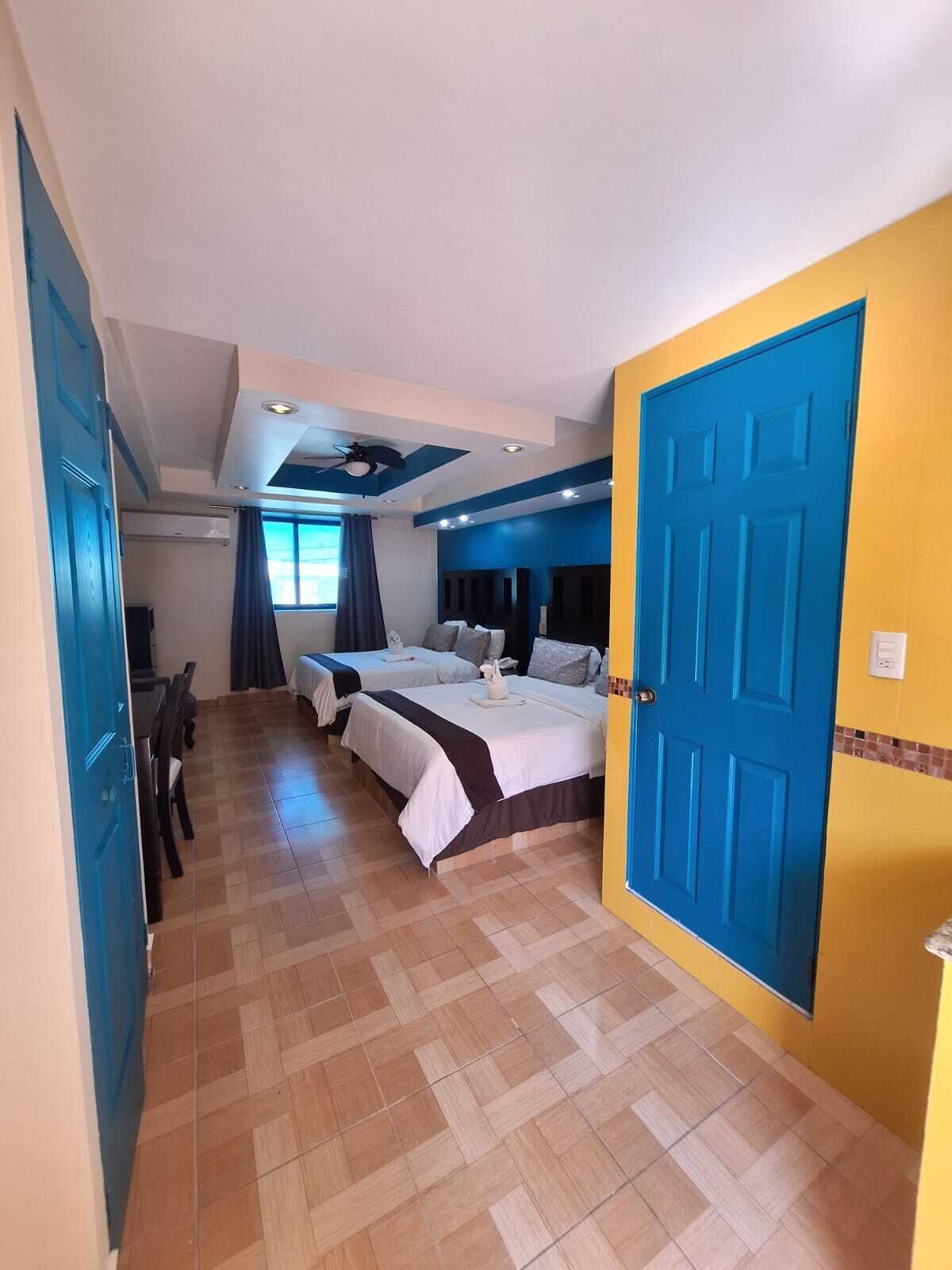 A hotel room with two beds, a dining area, and a bathroom.