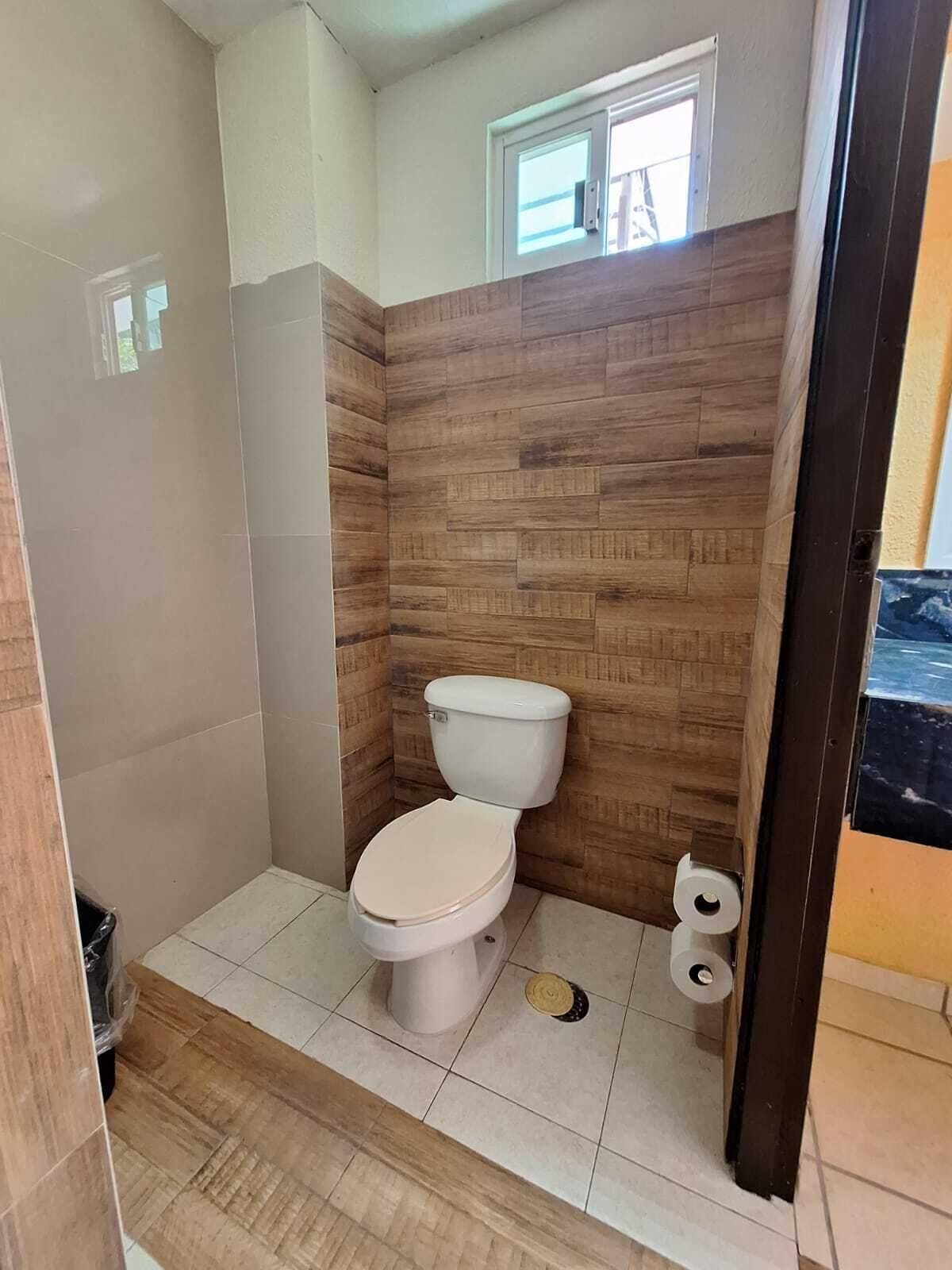 A small bathroom with a toilet, a window, and a shower area.