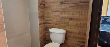 A small bathroom with a toilet, a window, and a shower area.