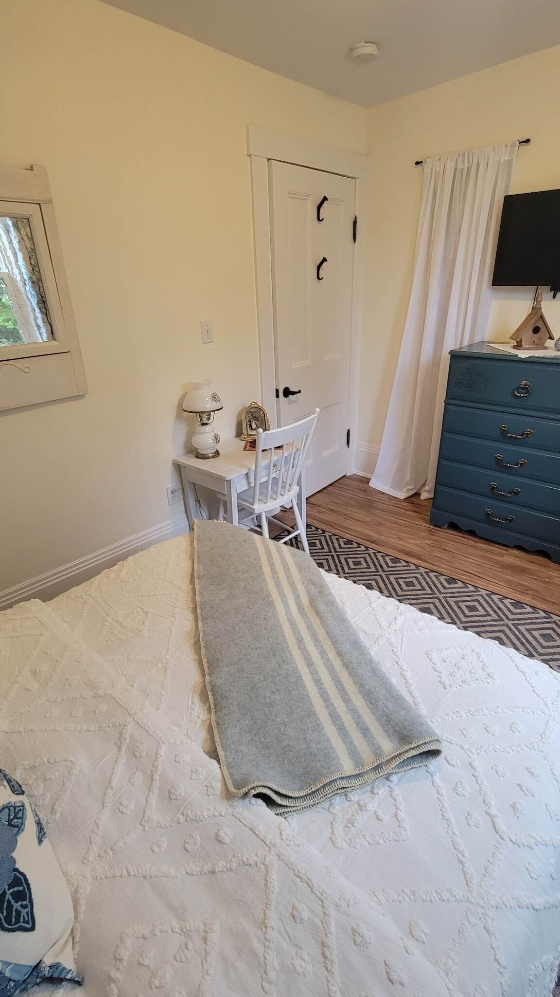 A bedroom with a bed, a desk, a chair, a dresser, and a window.