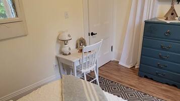 A bedroom with a bed, a desk, a chair, a dresser, and a window.