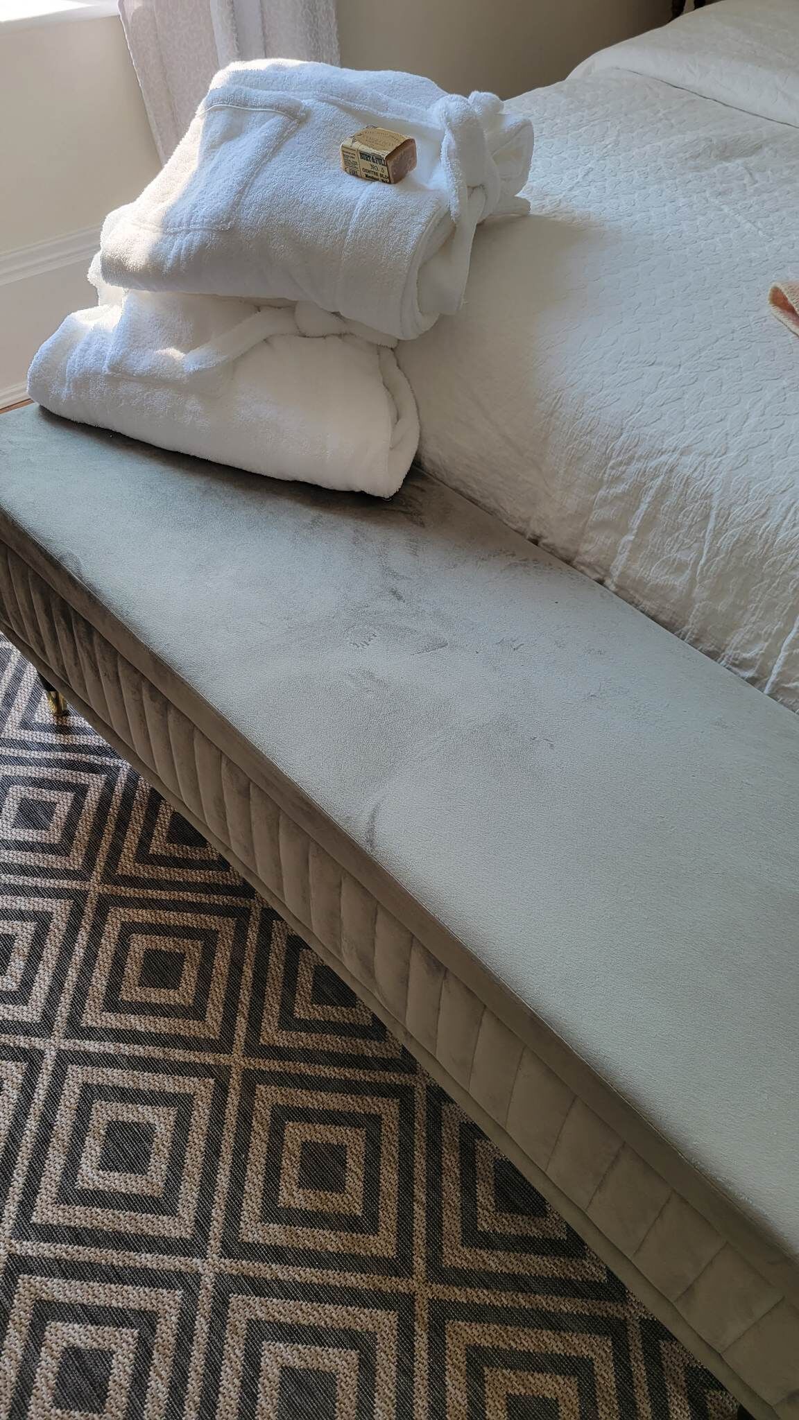 Un lit avec un tapis à motifs, une couverture blanche et une petite boîte posée sur le lit.