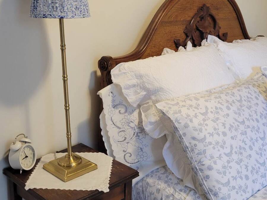 Quarto com cama de madeira, mesa de cabeceira com abajur, relógio e duas fotos emolduradas na parede.