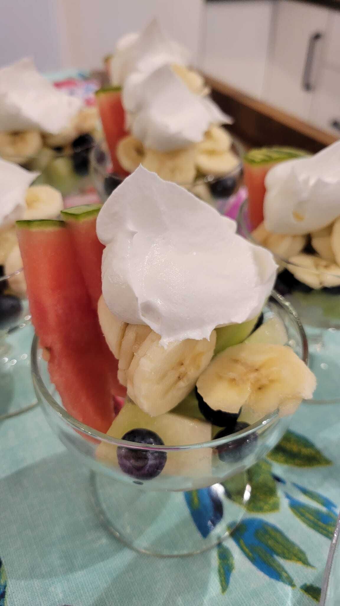 A dessert with whipped cream, watermelon, and bananas in a glass.