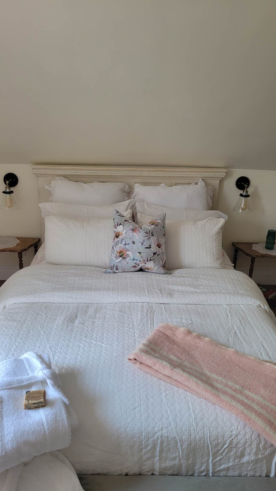 A neatly made bed with white linens and a floral pillow, two bedside tables with lamps, and a pink towel on the bed.