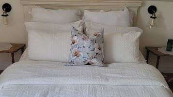 A neatly made bed with white linens and a floral pillow, two bedside tables with lamps, and a pink towel on the bed.