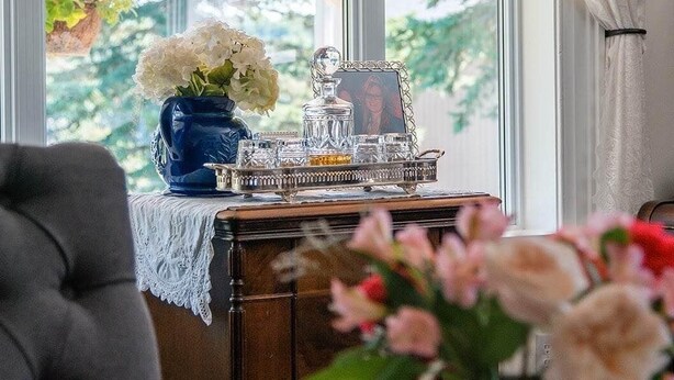 Una habitación con un ventanal grande, una mesa con un florero y una bandeja decorativa con cristalería.