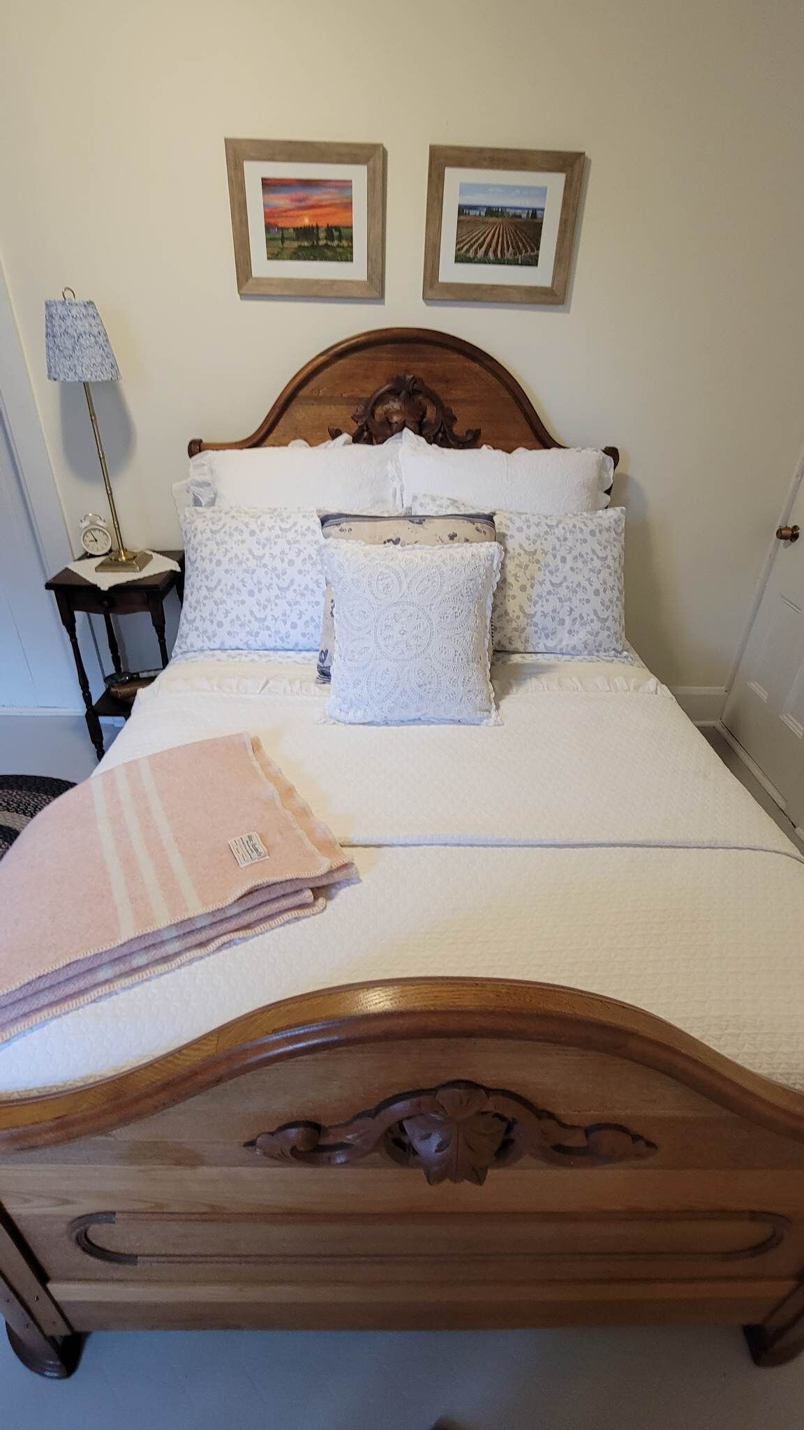 A neatly made bed with a wooden headboard, white linens, and a decorative pillow. There are two framed pictures on the wall above the bed.