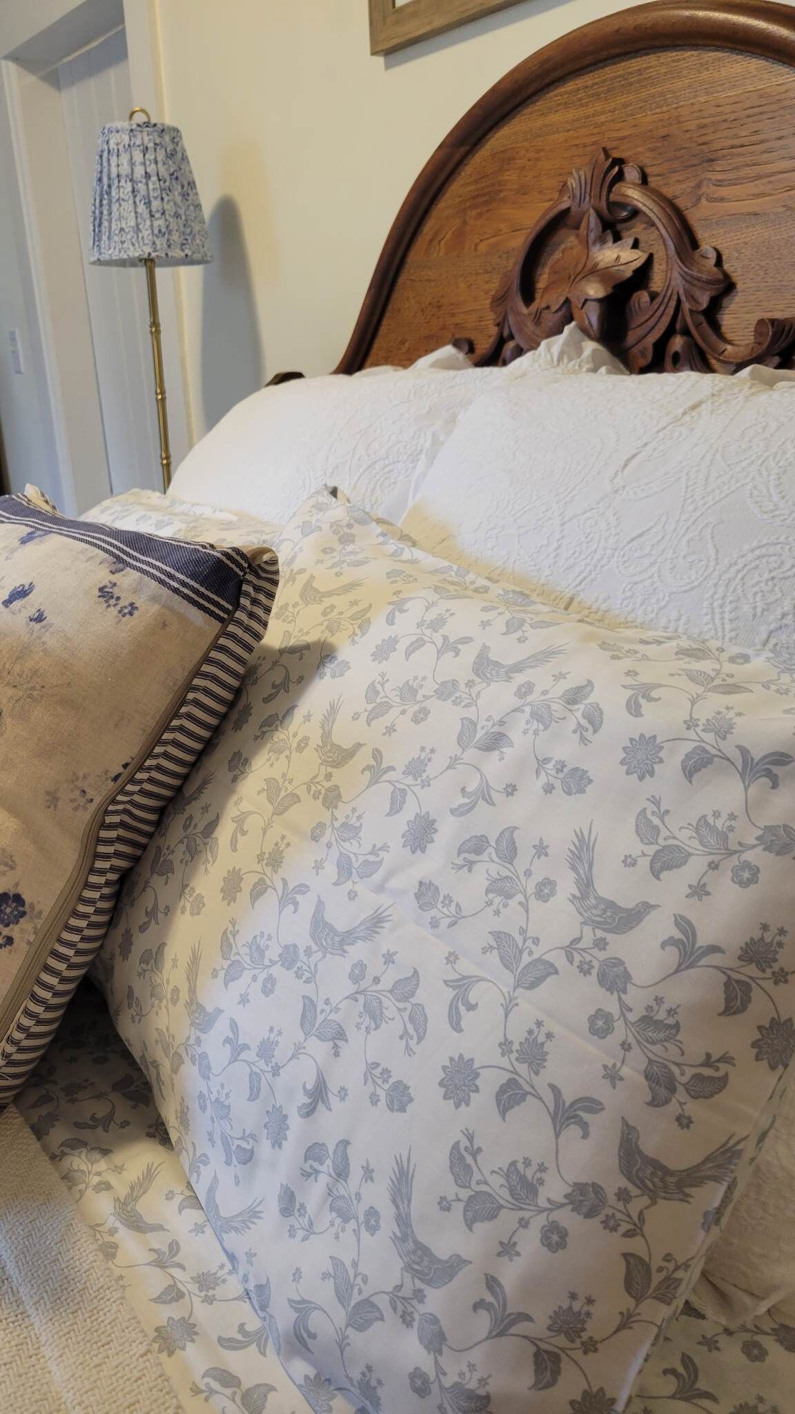 Uma cama com colcha e almofadas estampadas com flores, uma cabeceira de madeira e uma luminária em uma mesa de cabeceira.
