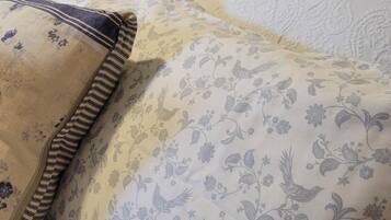 Uma cama com colcha e almofadas estampadas com flores, uma cabeceira de madeira e uma luminária em uma mesa de cabeceira.