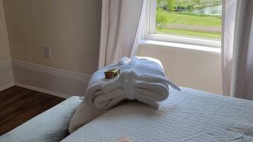 A neatly made bed with a folded towel and a pink towel on a textured white bedspread.