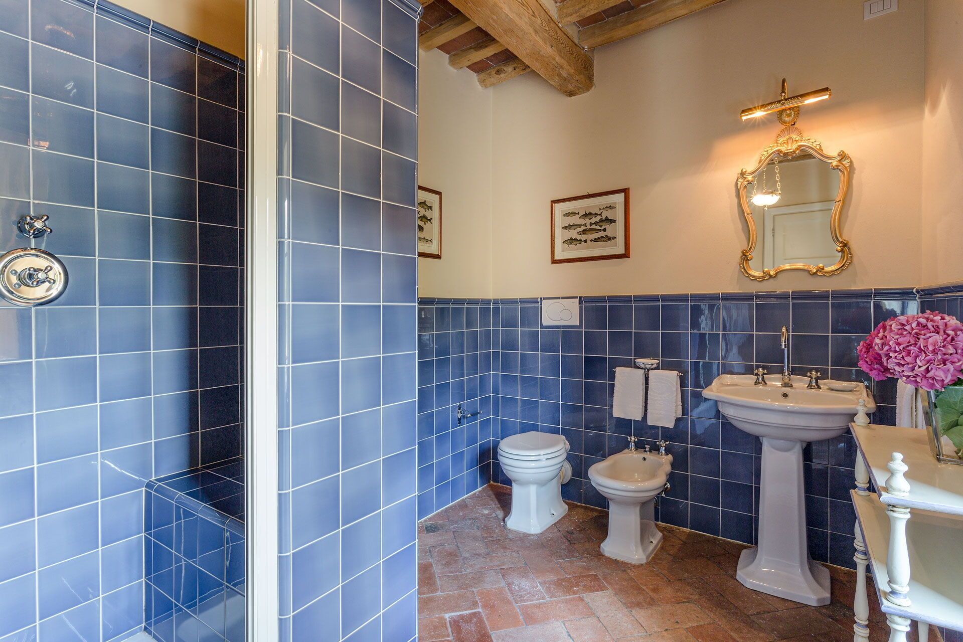 A bathroom with blue tiles, a white sink, a bidet, and a toilet.