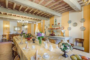 Comedor con una larga mesa dispuesta para una comida, que incluye una araña, platos decorativos y un espejo.