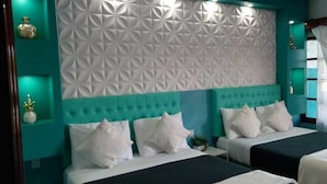 Een hotelkamer met twee bedden, teal muren en een decoratief wit paneel op het hoofdeinde.