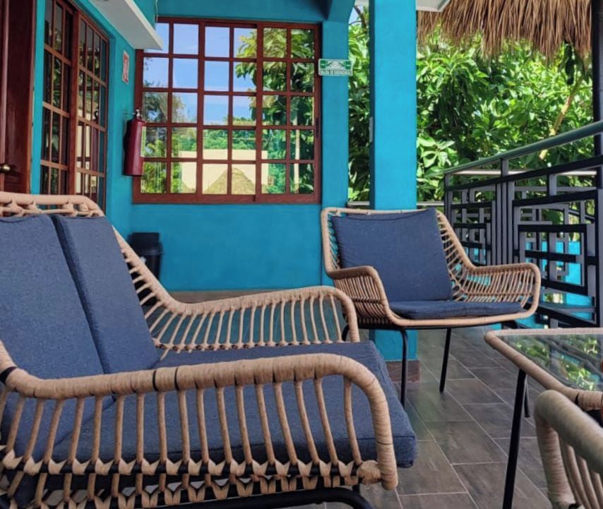 A balcony with wicker chairs and a glass table, overlooking lush greenery.