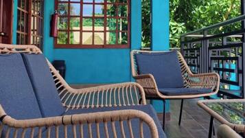 A balcony with wicker chairs and a glass table, overlooking lush greenery.