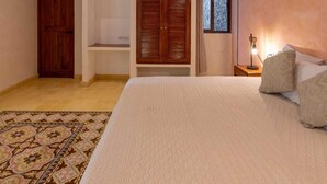 A bedroom with a bed, a ceiling fan, a window, and a wooden door. - Casa Pakal (Valladolid)