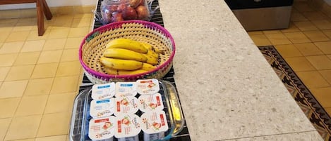 Un piano di lavoro in cucina con una macchina da caffè, un tostapane e un fornello. Si vedono anche cestini di frutta e vasetti di yogurt.