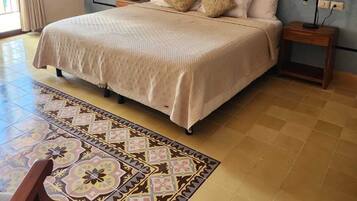 Un dormitorio con una cama grande, dos mesitas de noche, un tapete estampado y una ventana con cortinas.