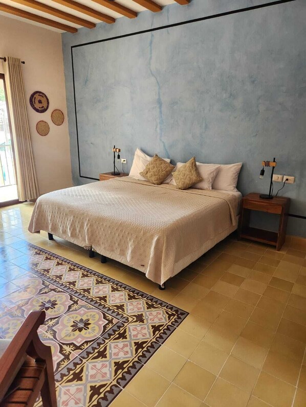 A bedroom with a large bed, two bedside tables, a patterned rug, and a window with curtains. - Casa Pakal (Valladolid)