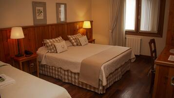 A hotel room with a large bed, two bedside tables with lamps, a wooden headboard, a window with curtains, and a radiator.