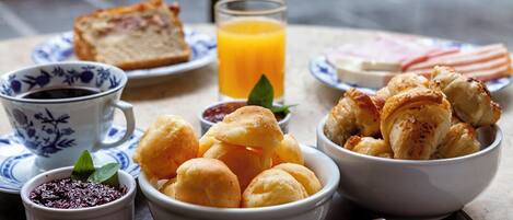 Una mesa de desayuno con pan, cruasanes, un vaso de zumo de naranja y una taza de café.
