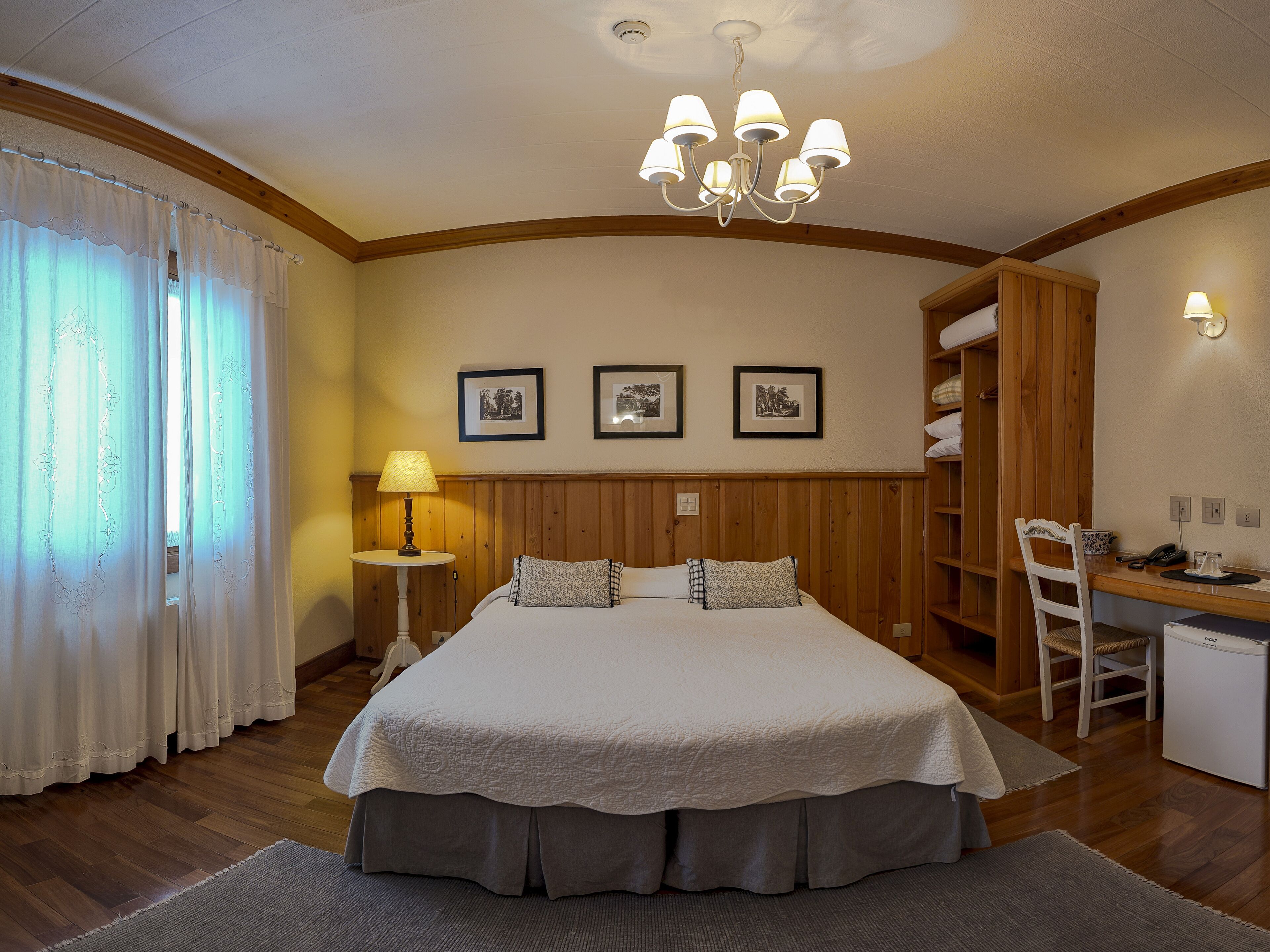 A bedroom with a large bed, a desk, a chair, a wardrobe, and a chandelier.