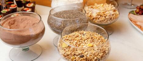 A variety of food items including chocolate mousse, chia seeds, and granola in clear glass bowls on a countertop.