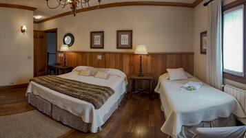 Habitación de hotel con dos camas, piso de madera, una araña y cuadros en las paredes.