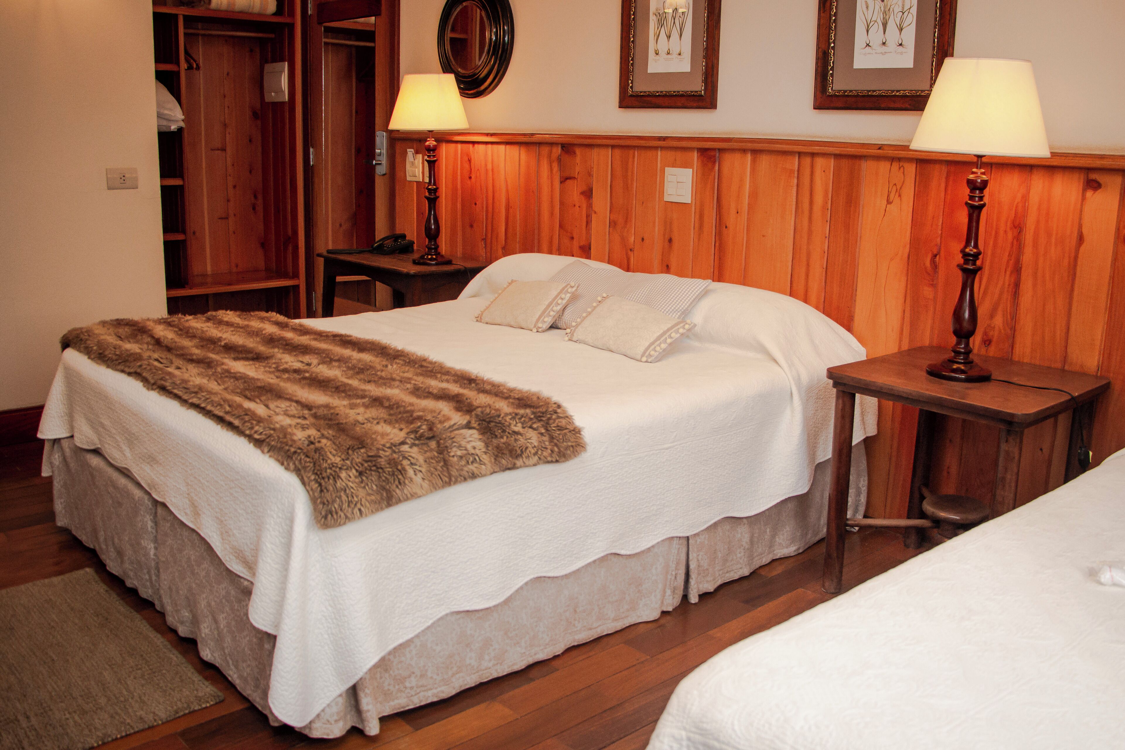 A hotel room with a large bed, a wooden wardrobe, two bedside tables with lamps, and a framed picture on the wall.