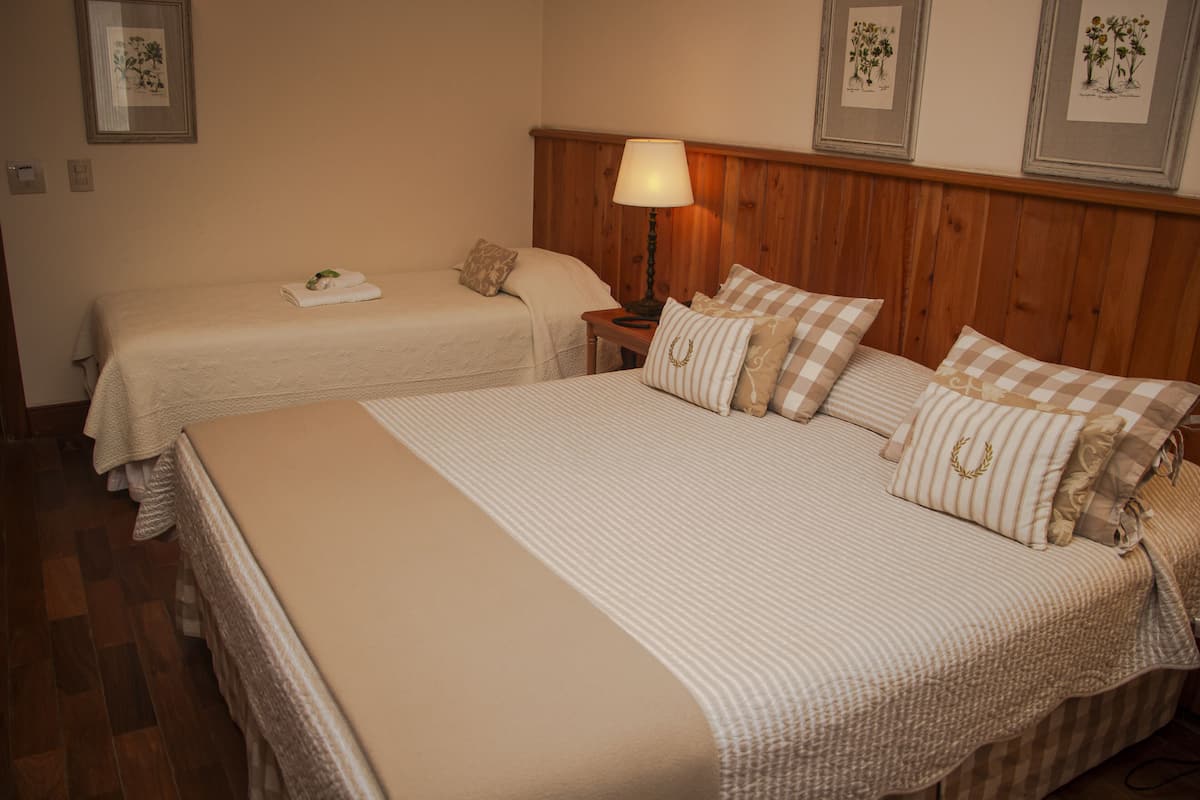 Quarto de hotel com duas camas de solteiro, cabeceira de madeira, mesa de cabeceira com abajur e quadros com ilustrações botânicas na parede.