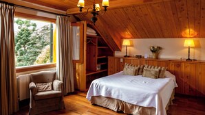 Un dormitorio con techo de madera, cama con ropa de cama blanca, una silla y una ventana con cortinas.
