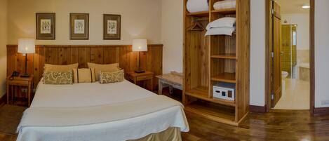 A spacious bedroom with a large bed, wooden headboard, bedside lamps, a wooden wardrobe, and a walk-in closet.