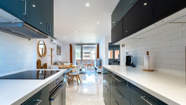 Una cocina moderna con una isla central, electrodomésticos integrados y un rincón de comedor con sofá y sillas.