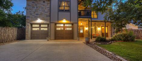 A two-story house with a stone facade, a balcony, and a well-lit entrance.