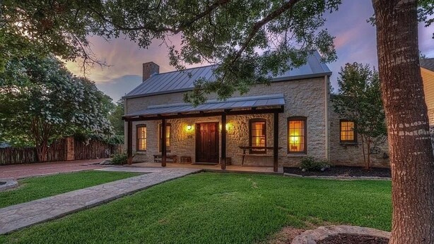 A stone house with a covered porch and a well-maintained lawn. - Cozy Haven | Shared Pool • Firepit • Hot Tub (Fredericksburg)