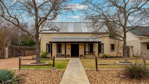 A stone building with a central entrance, surrounded by a gravel pathway and small plants. - Cozy Haven | Shared Pool • Firepit • Hot Tub (Fredericksburg)