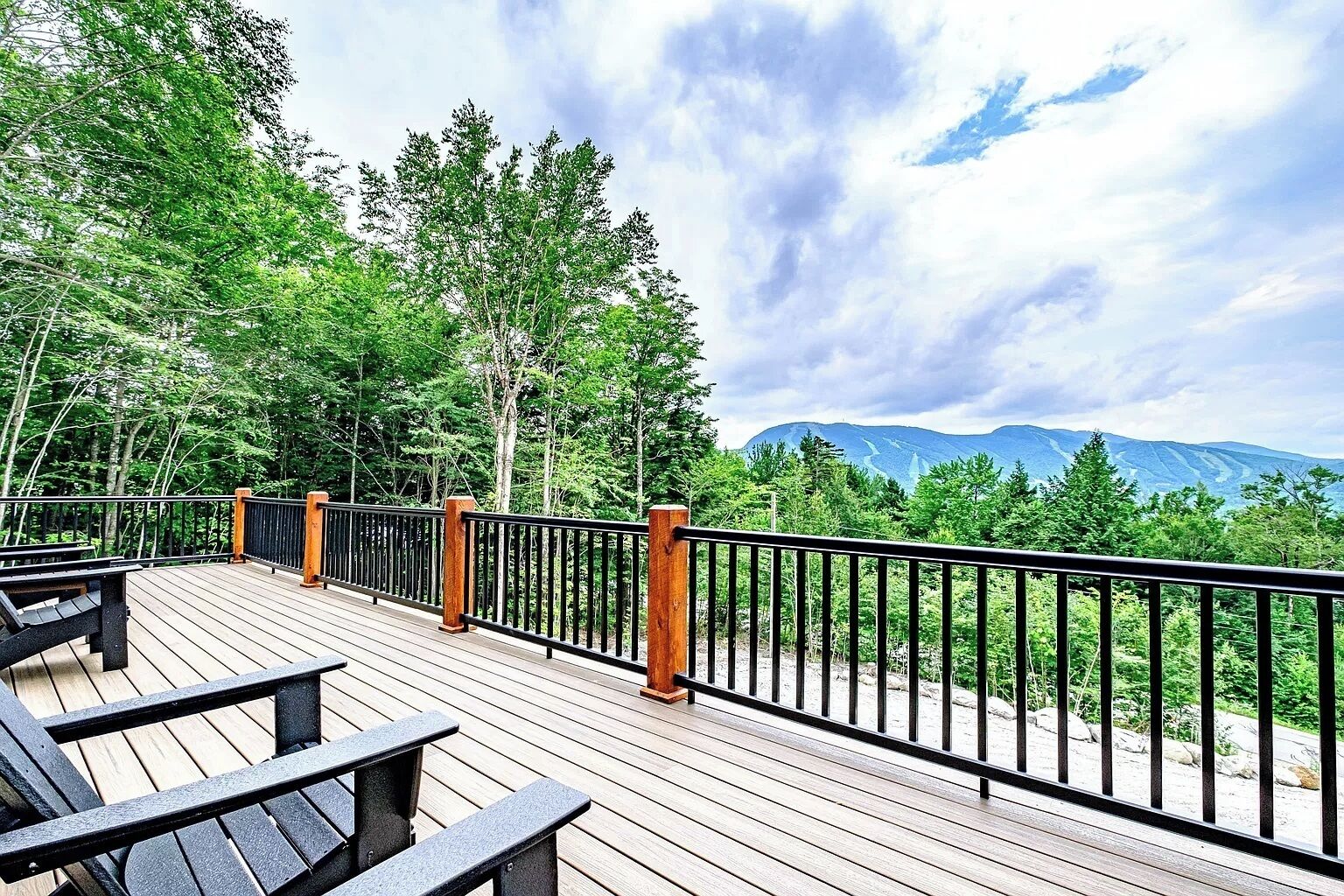 Une terrasse en bois avec des rampes en métal noir, entourée d’arbres et offrant une vue sur la montagne.